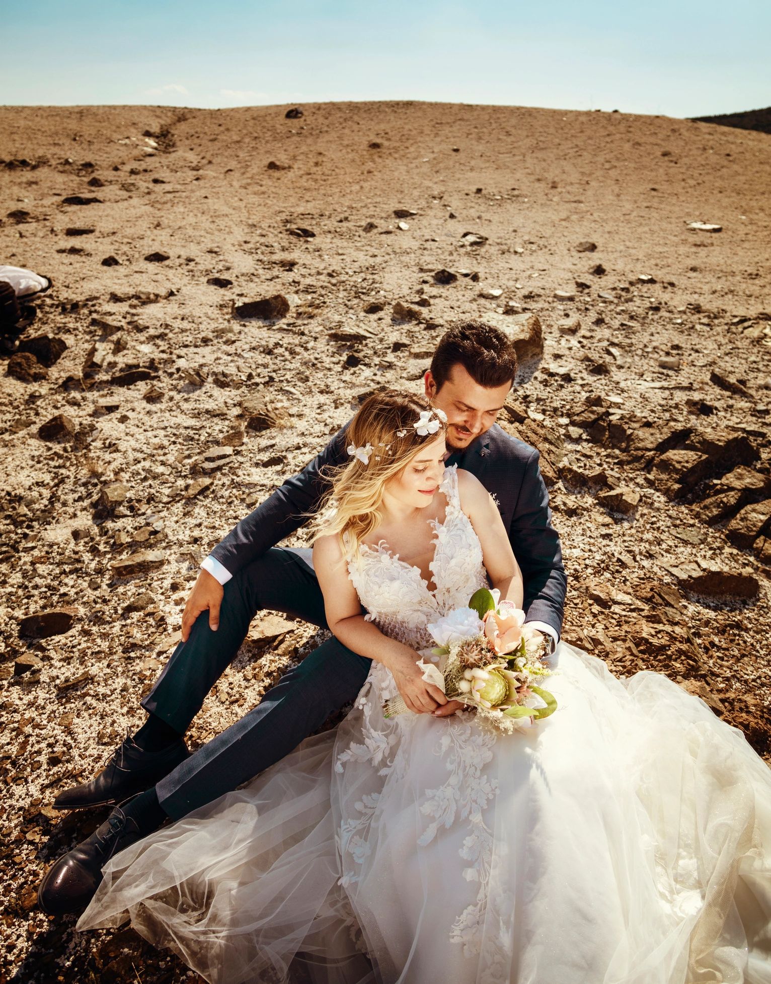 Bride and groom seated on a rock in an elegant outdoor portrait